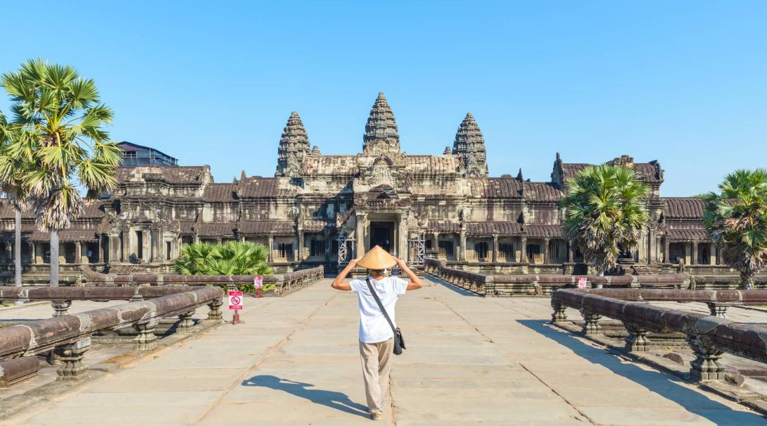 A lone woman walks on the large stone pathway towards the entrance of Angkor Wat