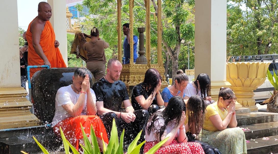 Eight people receive a water blessing from a Buddhist monk who stands behind them 
