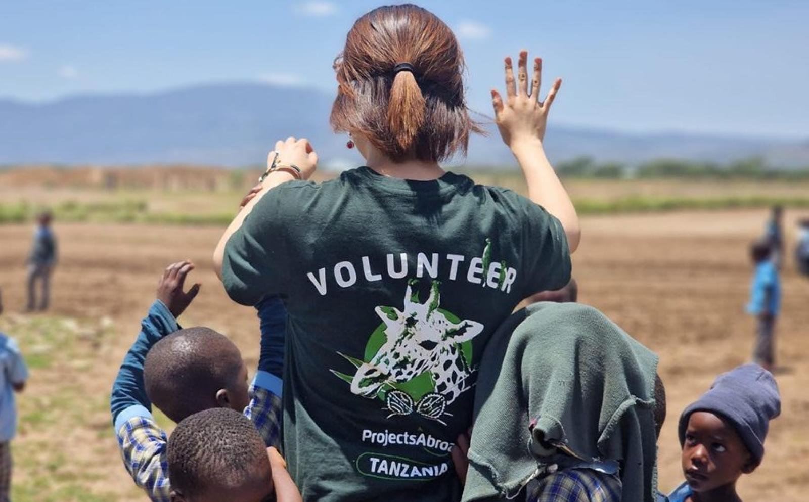 タンザニアの大地で子供たちとハイタッチをする日本人大学生ボランティア