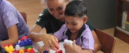 A volunteer working abroad with children spends time building blocks with a child to improve early childhood development.