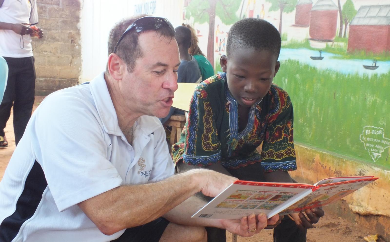An older volunteer reads to a child as part of his childcare volunteer work overseas