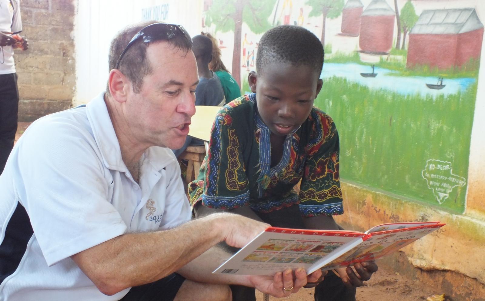 An older volunteer reads to a child as part of his childcare volunteer work overseas