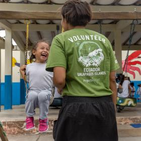 During volunteer work abroad with children in Ecuador a young child swings on the playground while a volunteer supervises