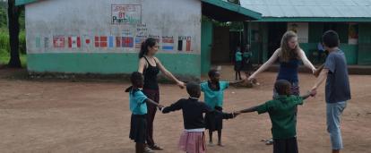 Group of teenage volunteers in Ghana play a game outdoors with children at a rural school.