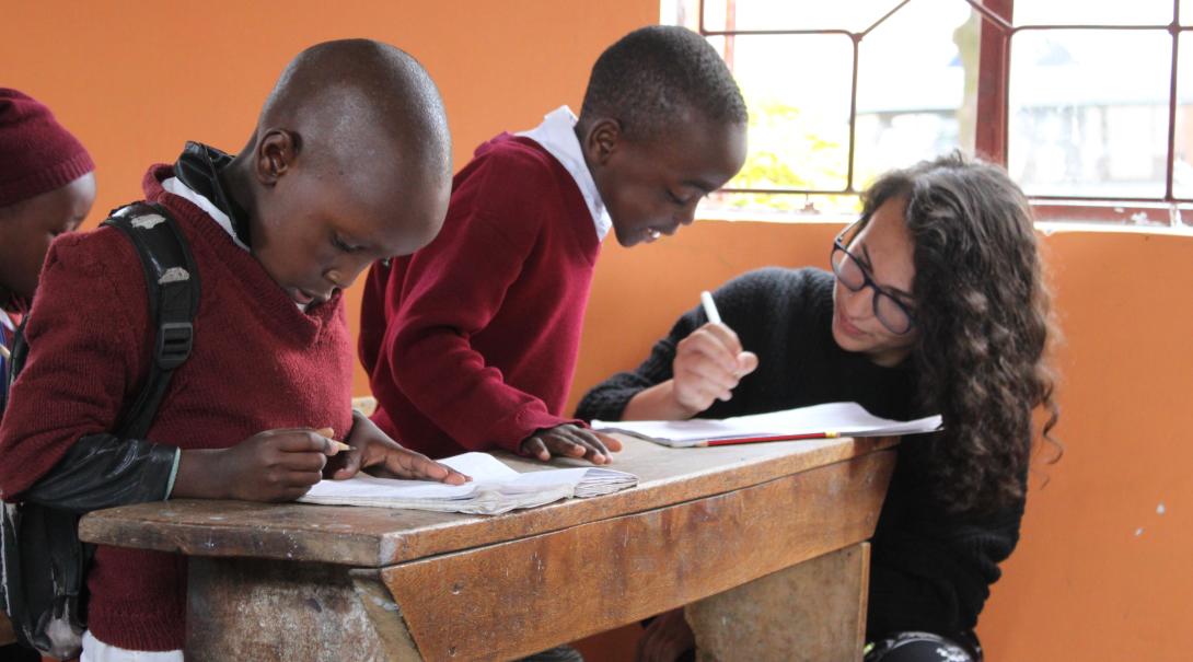 A volunteer teaching abroad helps children with their classwork in Tanzania. 