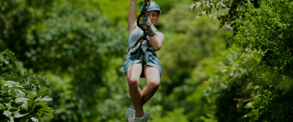 A female wearing a helmet ziplines above the canopy
