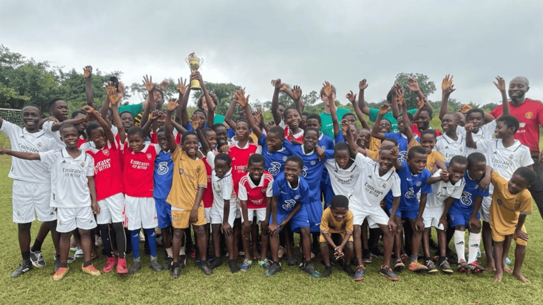 A group of 4 Projects Abroad volunteers in Ghana pose for a picture with the large group of children they were coaching in football. 