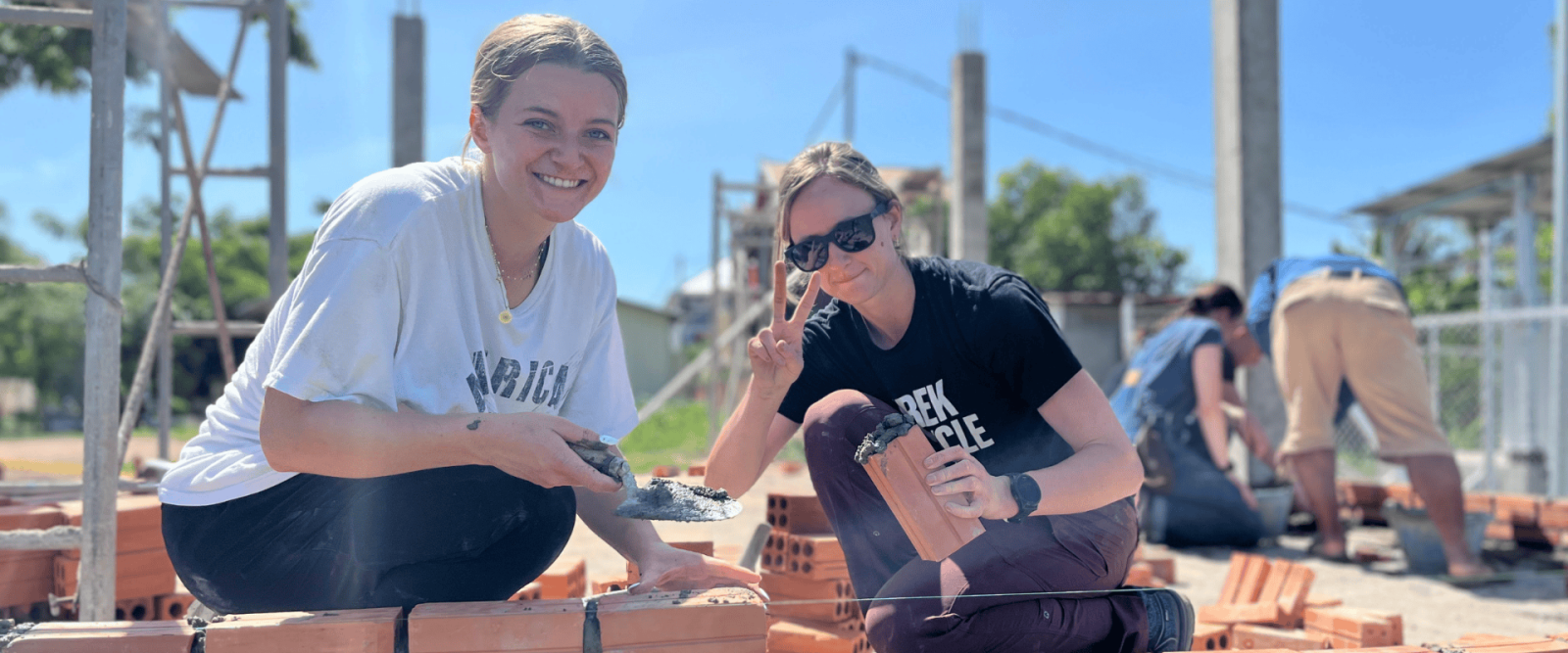 Two Projects Abroad volunteers constructing a building in Cambodia using bricks in sunny weather